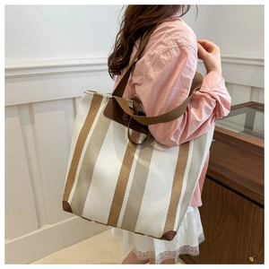 Detail of the large striped canvas tote bag showing the dark brown leather reinforced corners