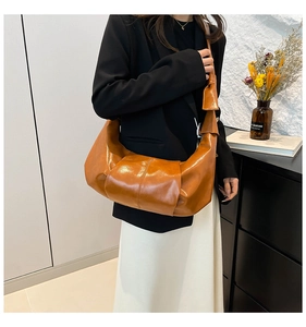 Detail view of caramel brown pleated shoulder bag with smooth glossy finish on model
