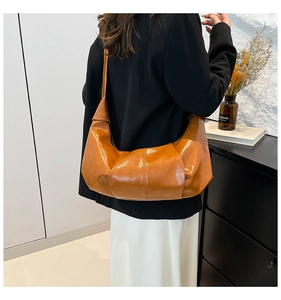 Detail of caramel brown crescent shoulder bag showing soft pleated glossy leather texture