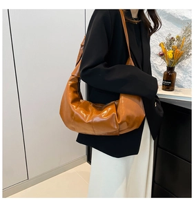 Brown pleated crescent bag made of glossy PU leather shown in a lifestyle model shot