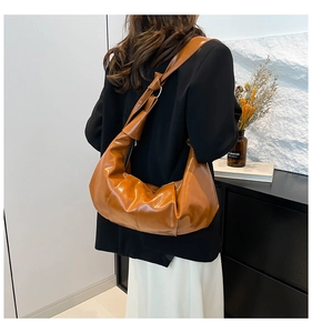Detail of a brown glossy leather shoulder bag featuring a pleated design and knotted strap