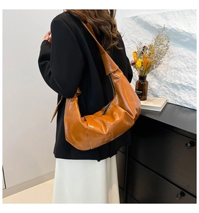 Close-up of caramel leather shoulder bag with vintage pleats and glossy finish on model