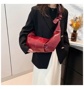 Detail of burgundy crescent bag featuring pleated leather texture and a knotted shoulder strap