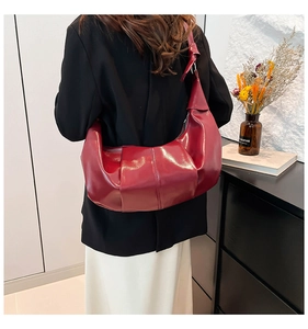 Detail of burgundy pleated leather shoulder bag with decorative knotted strap and glossy finish