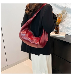Close-up of glossy dark red leather shoulder bag featuring wide strap and pleated details