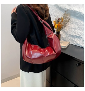 Detailed view of burgundy pleated leather cloud bag with knotted strap on a shoulder