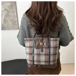 Detail of plaid tote bag featuring brown leather trim and circular metal N-logo buckle