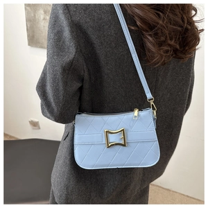 Détail d'un sac bandoulière matelassé bleu clair avec boucle dorée sur un manteau