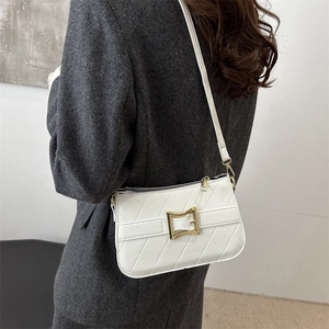 Sac à bandoulière matelassé blanc avec boucle dorée, porté sur un blazer gris chic