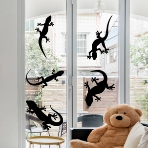 Dettaglio di cinque adesivi neri a silhouette di geco applicati su una porta di vetro