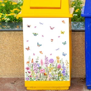 Detail of floral butterfly decals applied to a yellow trash can in a garden setting