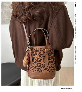 Detail of leopard print bucket bag with brown leather strap and plush charm on coat