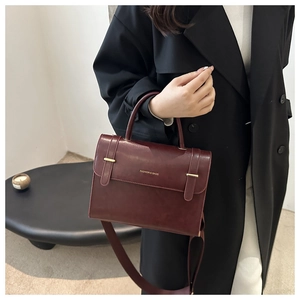 Détail d'un sac à main bordeaux en cuir avec boucles dorées et une poignée élégante