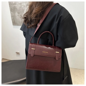 Détail d'un sac bandoulière en cuir bordeaux avec boucles dorées sur un manteau noir élégant