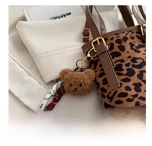 Detail of a brown plush bear charm with gold hardware attached to a leopard print bucket bag