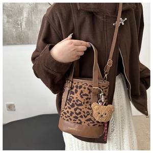Detail of leopard print bucket bag with plush bear charm and brown leather base
