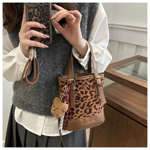 Detail of leopard print bucket bag featuring brown leather trim and a plush bear charm