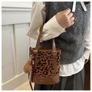Detailed view of leopard print bucket bag with brown leather accents and bear charm