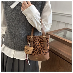 Close-up of leopard print bucket bag with plush bear charm and brown leather trim