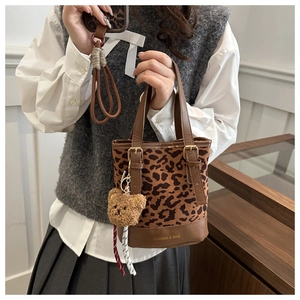 Detail of leopard print bucket bag with plush bear charm and leather handle accent