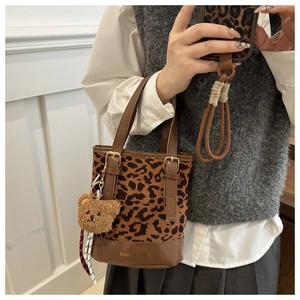 Detail of leopard print canvas bucket bag featuring brown leather trim and plush bear charm