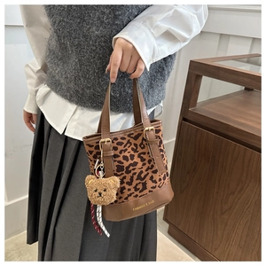 Detail of leopard print tote bag with brown leather handles and plush bear charm