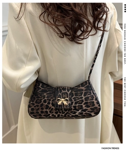 Detail shot of leopard print shoulder bag with gold bow clasp on beige suit background