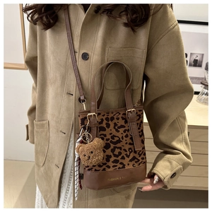 Detail of leopard print bucket bag with brown leather handles and plush bear charm