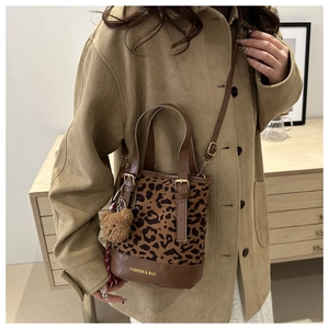 Detail of leopard print tote bag with brown leather base and plush bear charm
