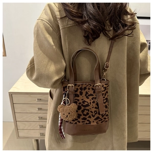 Detail of leopard print bucket bag with leather base and plush bear charm accessory