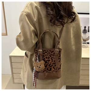 Detail showing leopard print canvas bucket bag with plush bear charm and leather handles