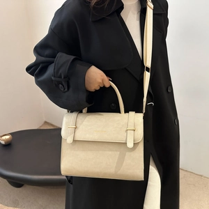 Sac bandoulière beige minimaliste avec poignée et large sangle sur manteau noir
