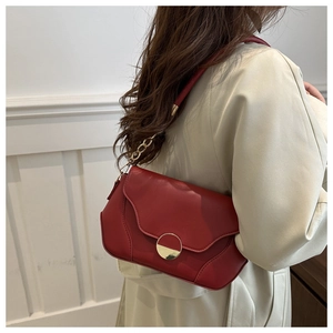 Detail of red crossbody bag with gold circular buckle and metallic chain strap detail