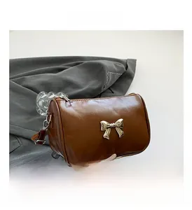 Détail d'un sac bandoulière en cuir marron avec un nœud décoratif en métal doré