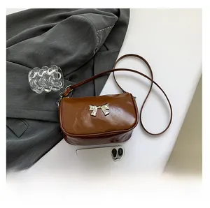 Détail d'un sac à bandoulière en cuir marron avec nœud argenté et texture plissée