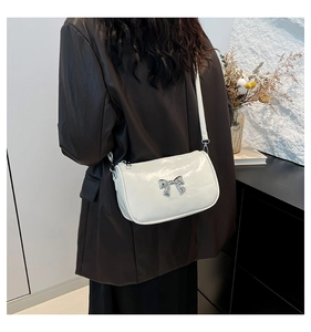 Détail d'un sac bandoulière en cuir verni blanc avec un nœud en métal argenté