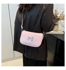 Sac bandoulière en cuir verni rose avec nœud argenté porté sur un blazer noir