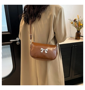 Sac bandoulière marron avec nœud argenté porté par un mannequin en trench-coat beige clair