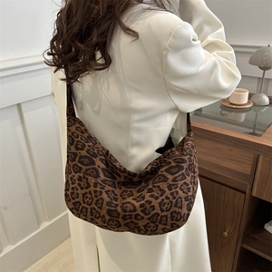 Large leopard print crescent tote bag worn by a model in a stylish white coat
