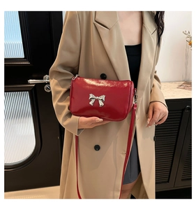 Sac bandoulière rouge en cuir avec nœud argenté porté par un mannequin en salle