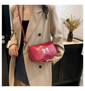 Détail du sac rouge avec nœud argenté et bandoulière réglable porté par un mannequin