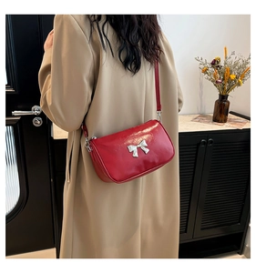 Détail du sac bandoulière rouge brillant avec un nœud métallique argenté sur le devant