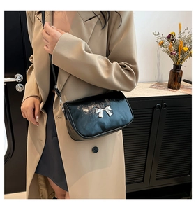 Vue détaillée du sac coquille noir avec nœud argenté porté sur un manteau beige