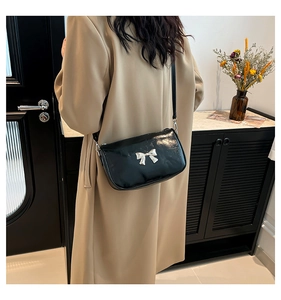 Détail du sac à bandoulière en cuir verni noir avec un nœud en métal argenté