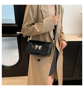 Détail du sac bandoulière noir avec nœud argenté porté sur un blazer beige chic