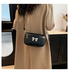 Détail d'un sac coquillage en cuir verni noir avec boucle nœud argenté sur un mannequin