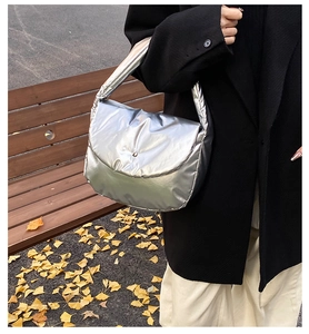 Outdoor street shot of a glossy silver padded puffer shoulder bag with metallic finish