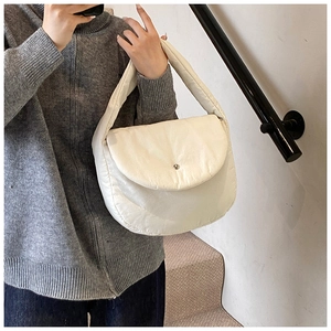 Detail of white puffer shoulder bag featuring quilted texture and silver metal button snap