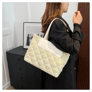 Detail view of beige quilted tote bag with white flap worn by model in black trench coat