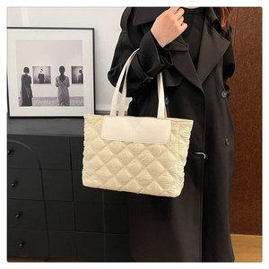 Detail view of a beige quilted tote bag with diamond pattern shown on a female model